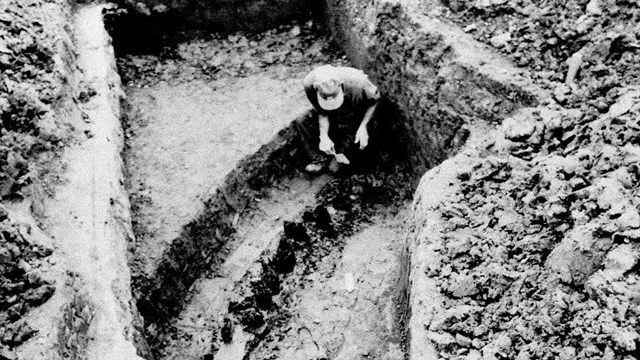 A man in a ditch looking at the remains of the original Fort Necessity stockade